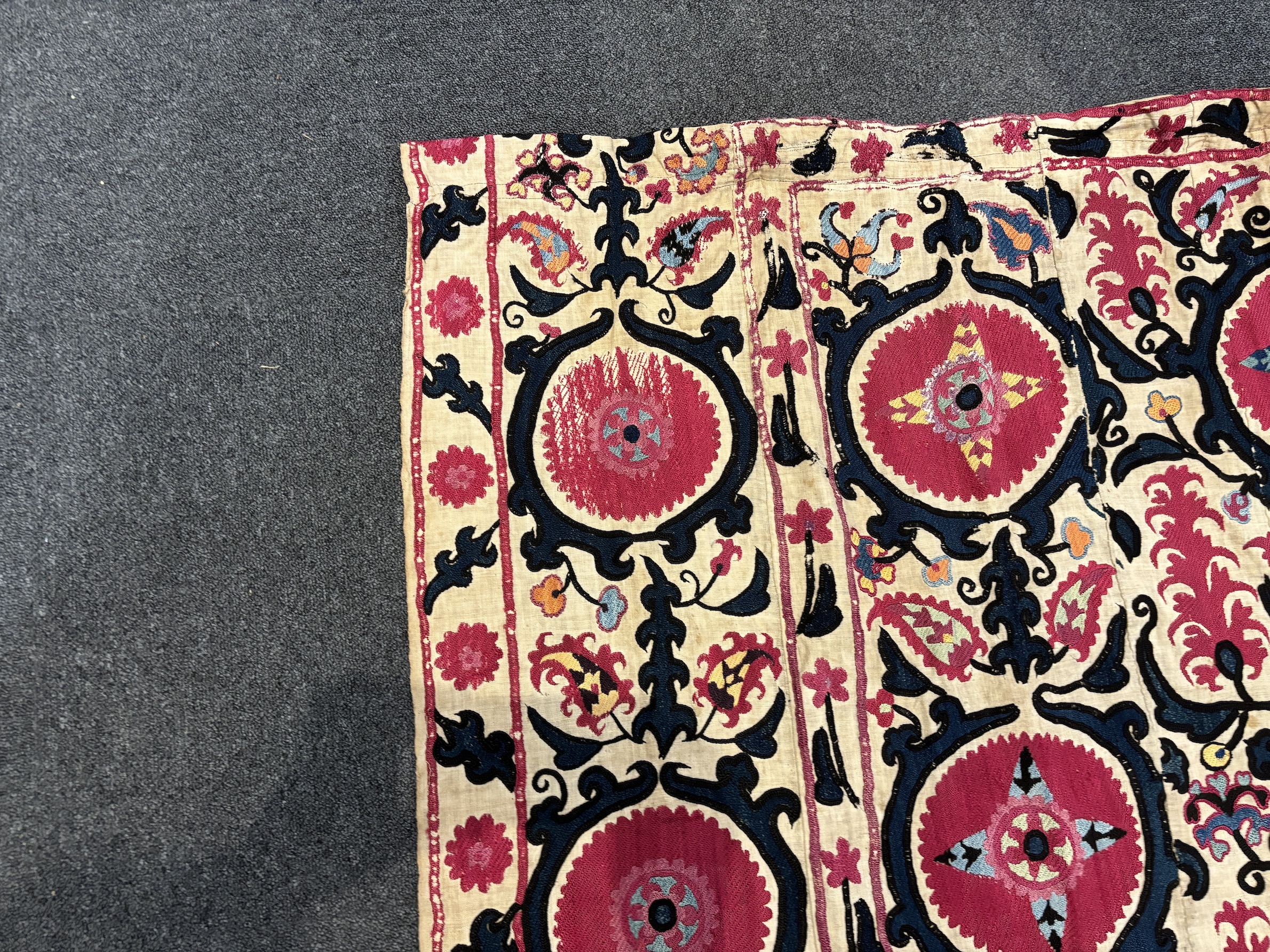 An 19th century Uzbek Suzani embroidered wall hanging, in two pieces, the main hanging sewn together as four panels, together with a fifth matching border, being detached, embroidered with large bold floral motifs, in ri
